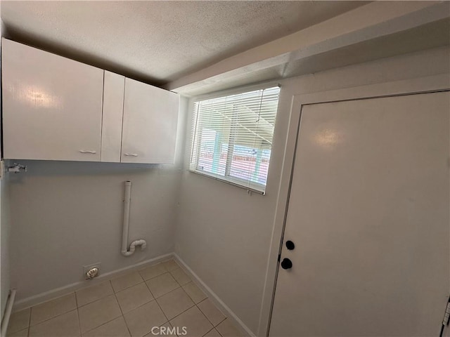 laundry room featuring cabinets, a textured ceiling, and light tile patterned floors