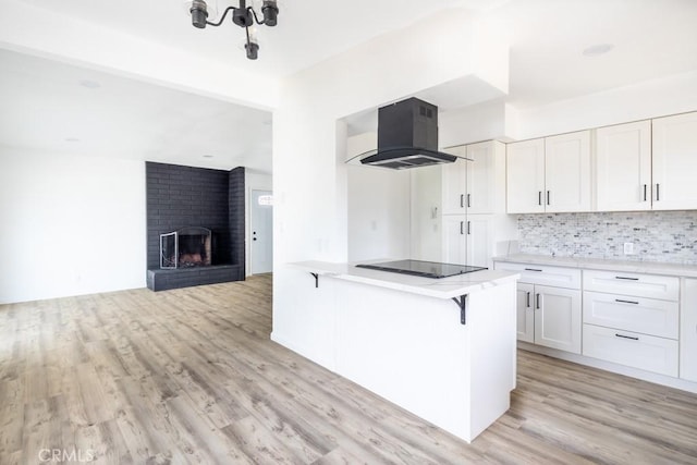 kitchen featuring island range hood, white cabinetry, a kitchen breakfast bar, black electric stovetop, and light wood-type flooring