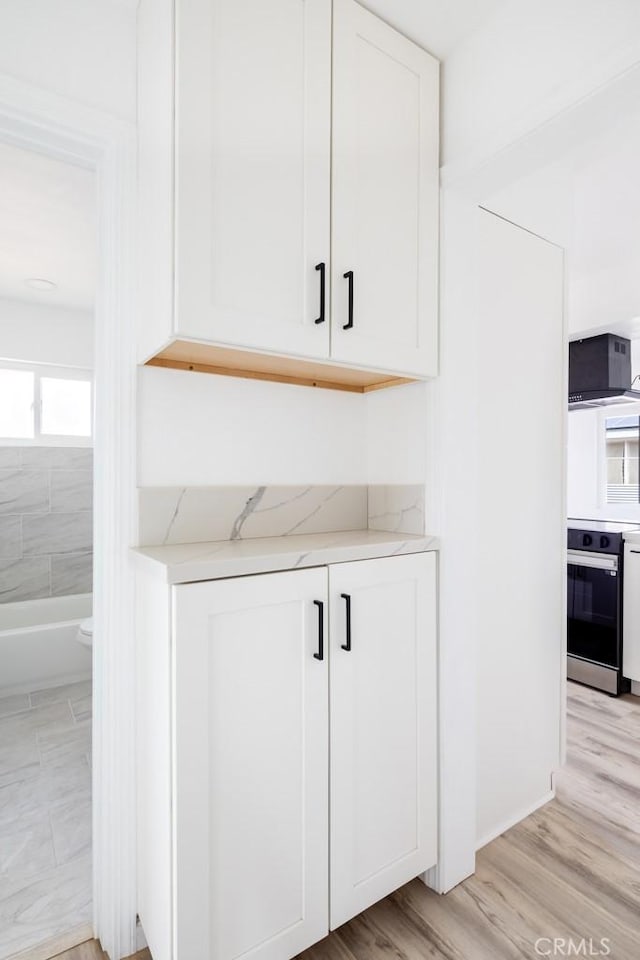 interior space with range with electric cooktop, light wood-type flooring, light stone counters, and white cabinets