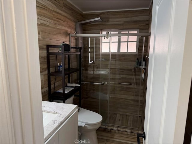 bathroom with vanity, toilet, an enclosed shower, and wood walls