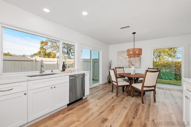 kitchen with pendant lighting, sink, white cabinets, stainless steel dishwasher, and light hardwood / wood-style floors