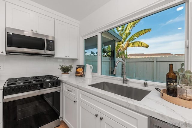 kitchen featuring gas range, white cabinetry, light stone countertops, and sink