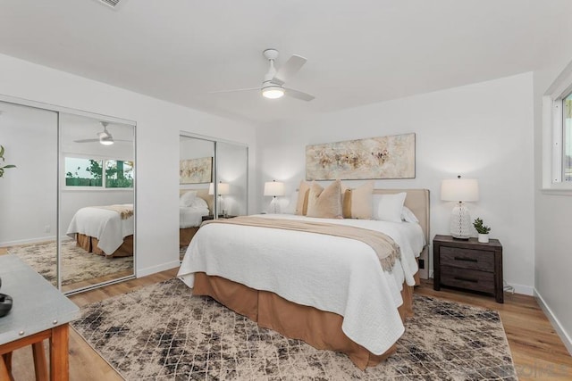 bedroom with two closets, light hardwood / wood-style flooring, and ceiling fan