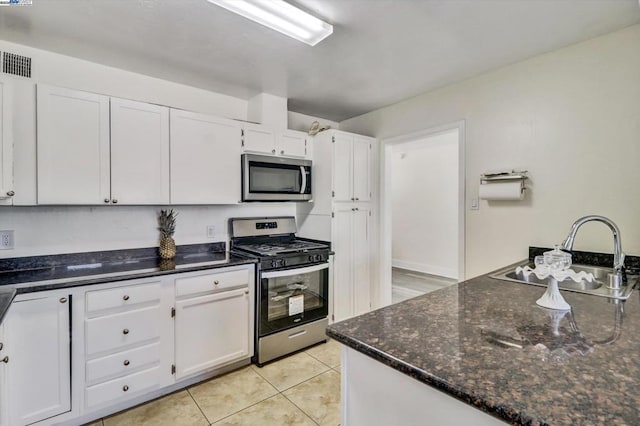 kitchen with light tile patterned flooring, sink, appliances with stainless steel finishes, dark stone counters, and white cabinets