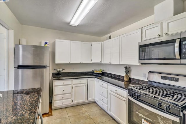 kitchen featuring light tile patterned flooring, appliances with stainless steel finishes, white cabinets, and dark stone counters