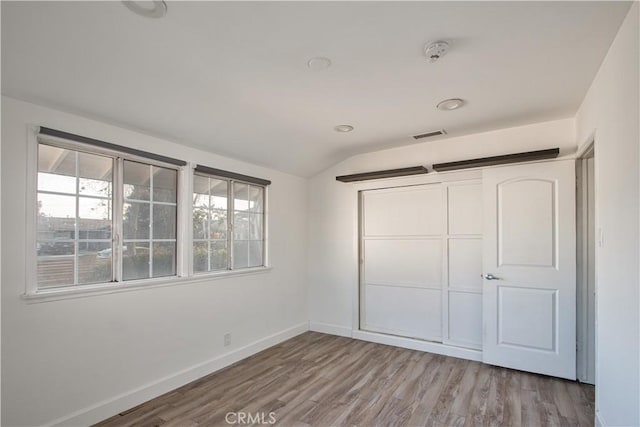 unfurnished bedroom with vaulted ceiling, light hardwood / wood-style floors, and a closet