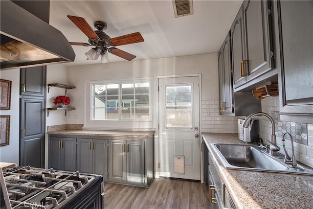 kitchen featuring sink, gray cabinetry, light hardwood / wood-style floors, gas stove, and decorative backsplash