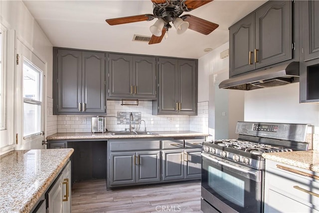 kitchen with sink, gray cabinetry, backsplash, light stone counters, and stainless steel gas range