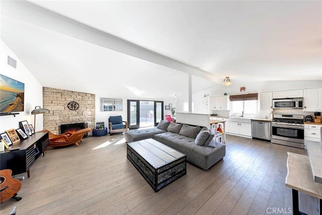 living area with vaulted ceiling, a fireplace, wood finished floors, and visible vents