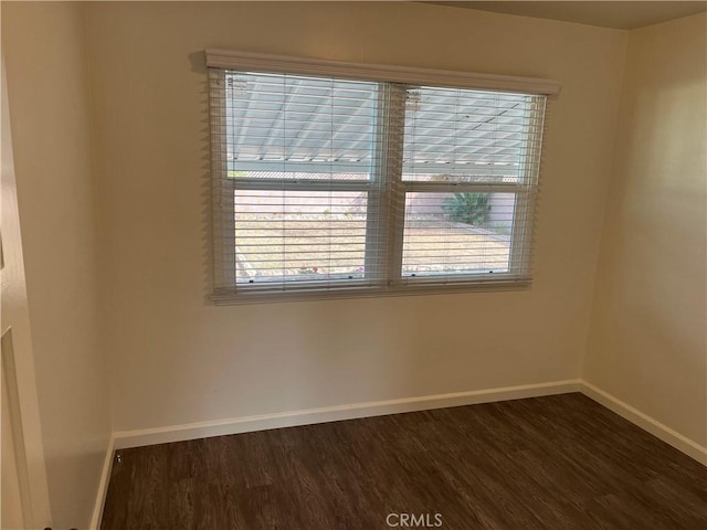 spare room featuring dark wood-type flooring and baseboards