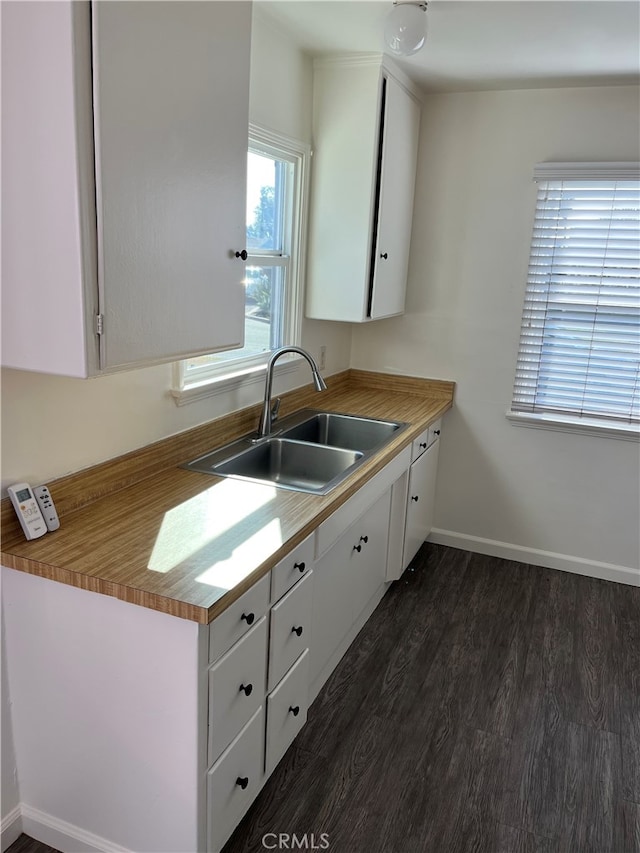 kitchen with a sink, white cabinetry, baseboards, light countertops, and dark wood finished floors