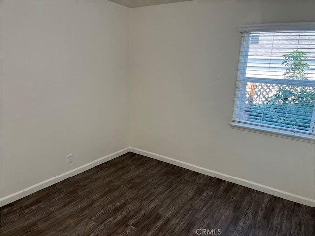 spare room featuring baseboards and dark wood finished floors