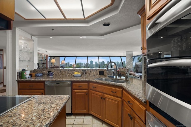 kitchen featuring light tile patterned flooring, appliances with stainless steel finishes, sink, light stone counters, and a raised ceiling