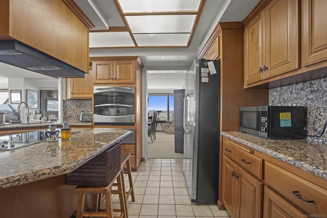 kitchen featuring sink, light tile patterned floors, a breakfast bar, appliances with stainless steel finishes, and stone countertops