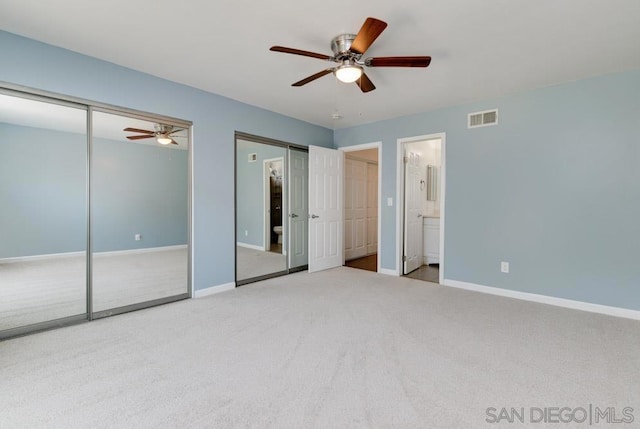 unfurnished bedroom with ceiling fan, carpet, two closets, and ensuite bath