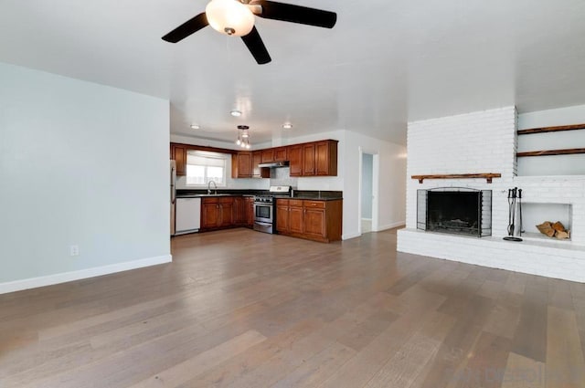 unfurnished living room with a brick fireplace, wood-type flooring, sink, and ceiling fan