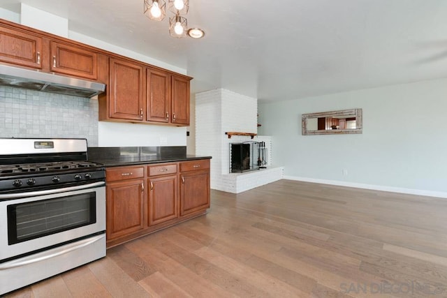 kitchen with tasteful backsplash, a fireplace, light hardwood / wood-style floors, and stainless steel gas stove