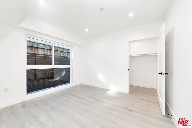 unfurnished bedroom with a spacious closet, light hardwood / wood-style flooring, and a closet