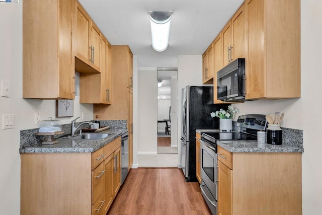 kitchen featuring appliances with stainless steel finishes, sink, dark stone counters, light hardwood / wood-style floors, and light brown cabinets