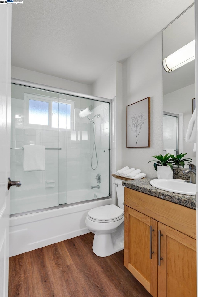 full bathroom with hardwood / wood-style flooring, vanity, shower / bath combination with glass door, and toilet