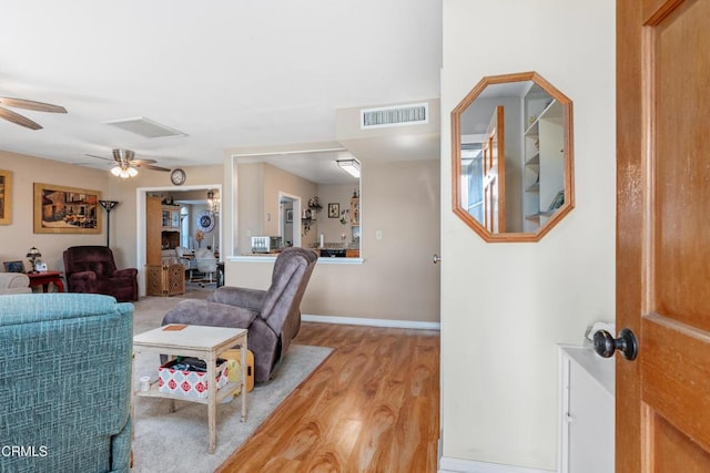 living area featuring visible vents, baseboards, a ceiling fan, and light wood finished floors