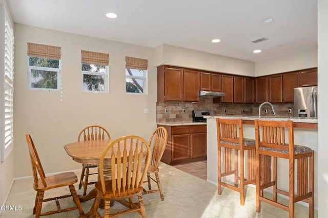 kitchen with light stone counters, backsplash, stainless steel fridge, and a healthy amount of sunlight