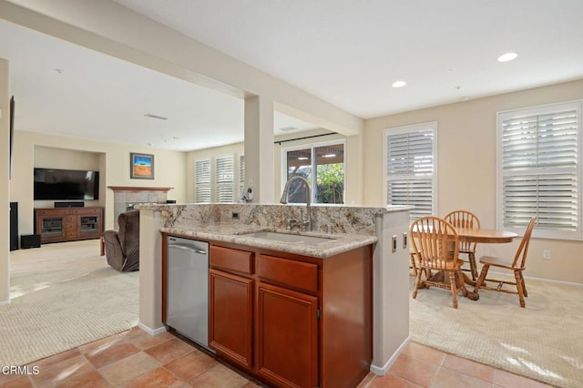 kitchen with sink, light stone counters, light carpet, dishwasher, and a tiled fireplace