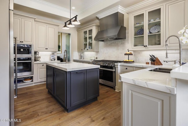 kitchen featuring sink, light stone counters, a center island with sink, stainless steel appliances, and wall chimney range hood