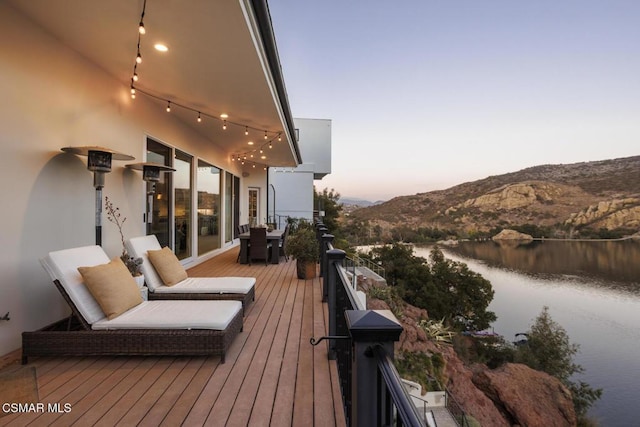 deck at dusk featuring a water and mountain view