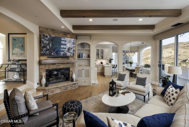 living room with a fireplace, beamed ceiling, and light wood-type flooring