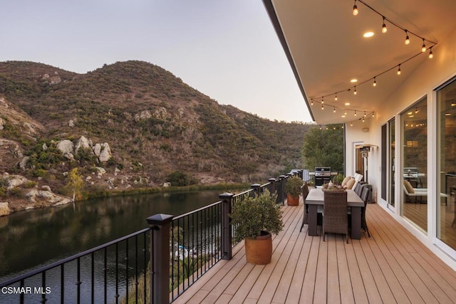 deck at dusk featuring a water and mountain view