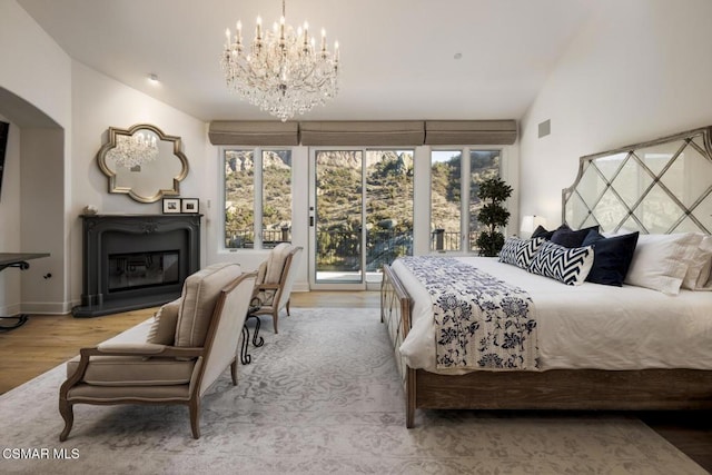 bedroom featuring an inviting chandelier, vaulted ceiling, hardwood / wood-style floors, and access to outside