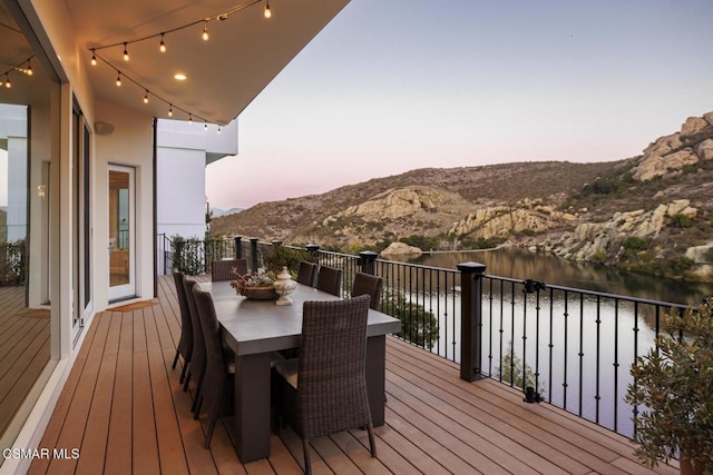 deck at dusk featuring a water and mountain view