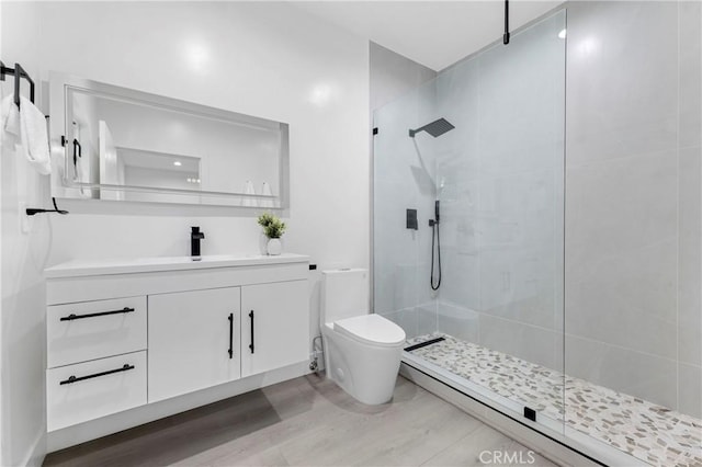 bathroom with toilet, wood finished floors, tiled shower, and vanity