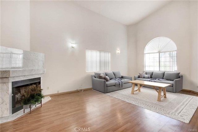 living room with a tiled fireplace, high vaulted ceiling, and light wood-type flooring