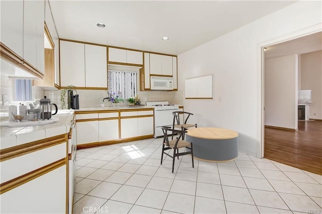 kitchen featuring light tile patterned flooring, sink, tasteful backsplash, white appliances, and white cabinets