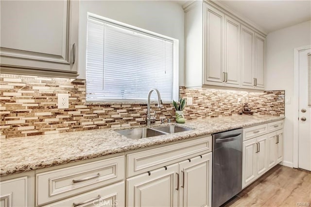 kitchen featuring sink, light stone counters, stainless steel dishwasher, light hardwood / wood-style floors, and backsplash