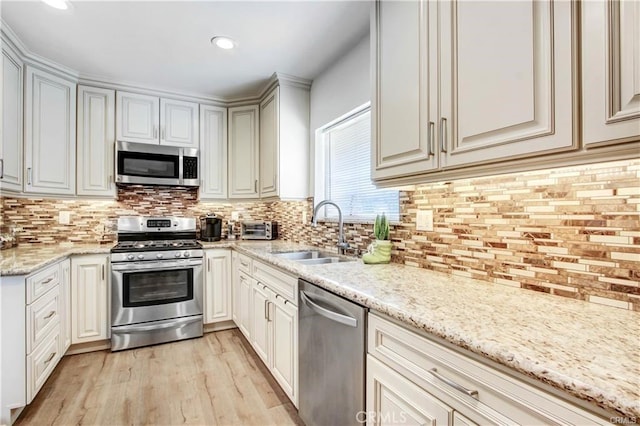 kitchen featuring sink, decorative backsplash, light hardwood / wood-style floors, light stone counters, and stainless steel appliances