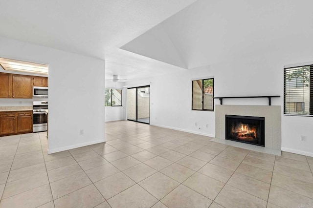 unfurnished living room with ceiling fan, a wealth of natural light, a tile fireplace, and light tile patterned floors