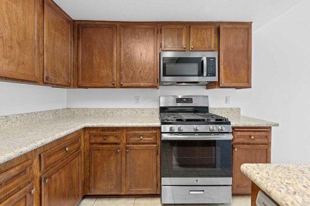 kitchen featuring stainless steel appliances, light tile patterned floors, and light stone counters