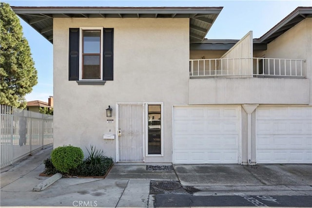 view of front of home featuring a balcony, a garage, fence, and stucco siding