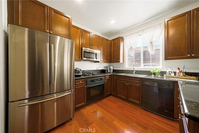 kitchen with sink, dark stone counters, dark hardwood / wood-style flooring, and black appliances