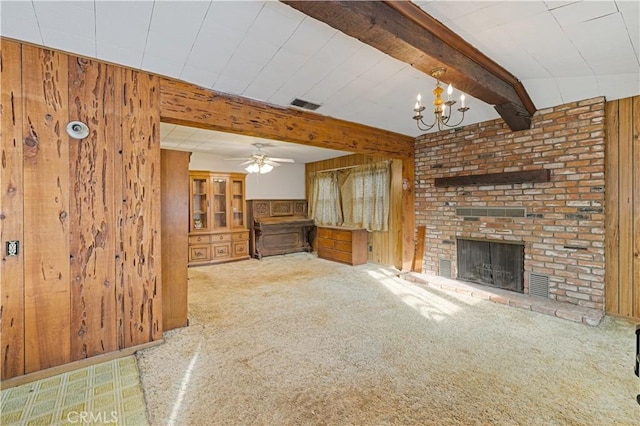 unfurnished living room with wood walls, light carpet, a brick fireplace, beamed ceiling, and ceiling fan with notable chandelier