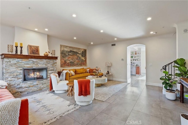 living area featuring arched walkways, recessed lighting, visible vents, a stone fireplace, and baseboards