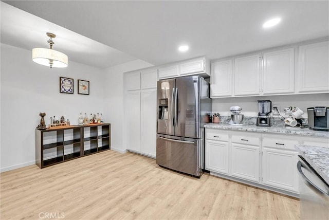 kitchen featuring appliances with stainless steel finishes, decorative light fixtures, white cabinetry, light stone countertops, and light wood-type flooring