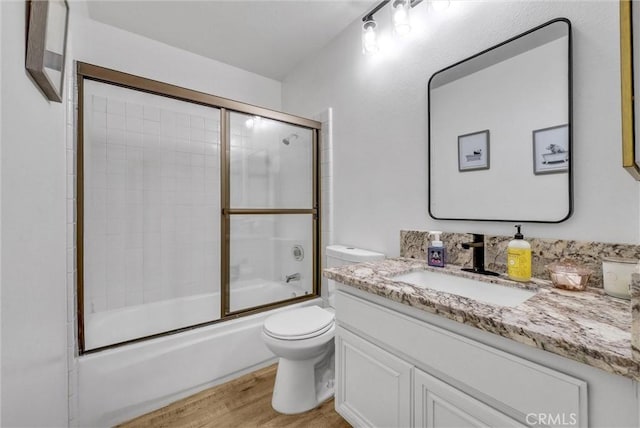 full bathroom with hardwood / wood-style flooring, vanity, toilet, and combined bath / shower with glass door