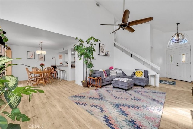 living room featuring ceiling fan with notable chandelier, a high ceiling, and light wood-type flooring