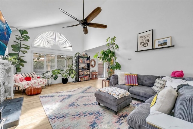 living room featuring a high ceiling, wood-type flooring, a fireplace, and ceiling fan