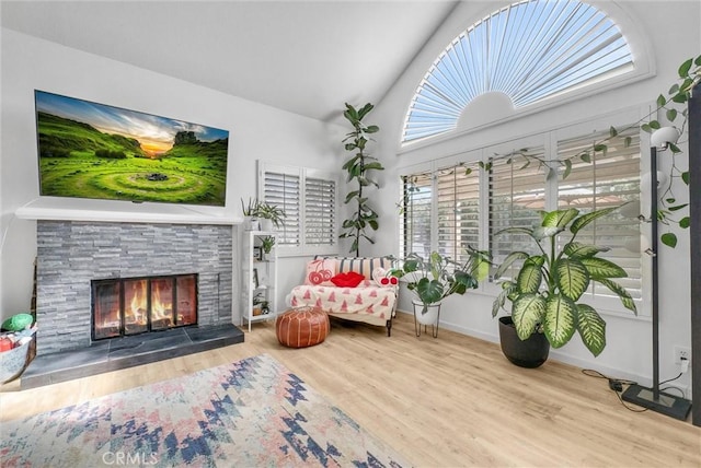 living area featuring a stone fireplace, wood-type flooring, and vaulted ceiling