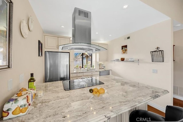 kitchen with appliances with stainless steel finishes, a kitchen breakfast bar, light stone counters, cream cabinets, and island range hood